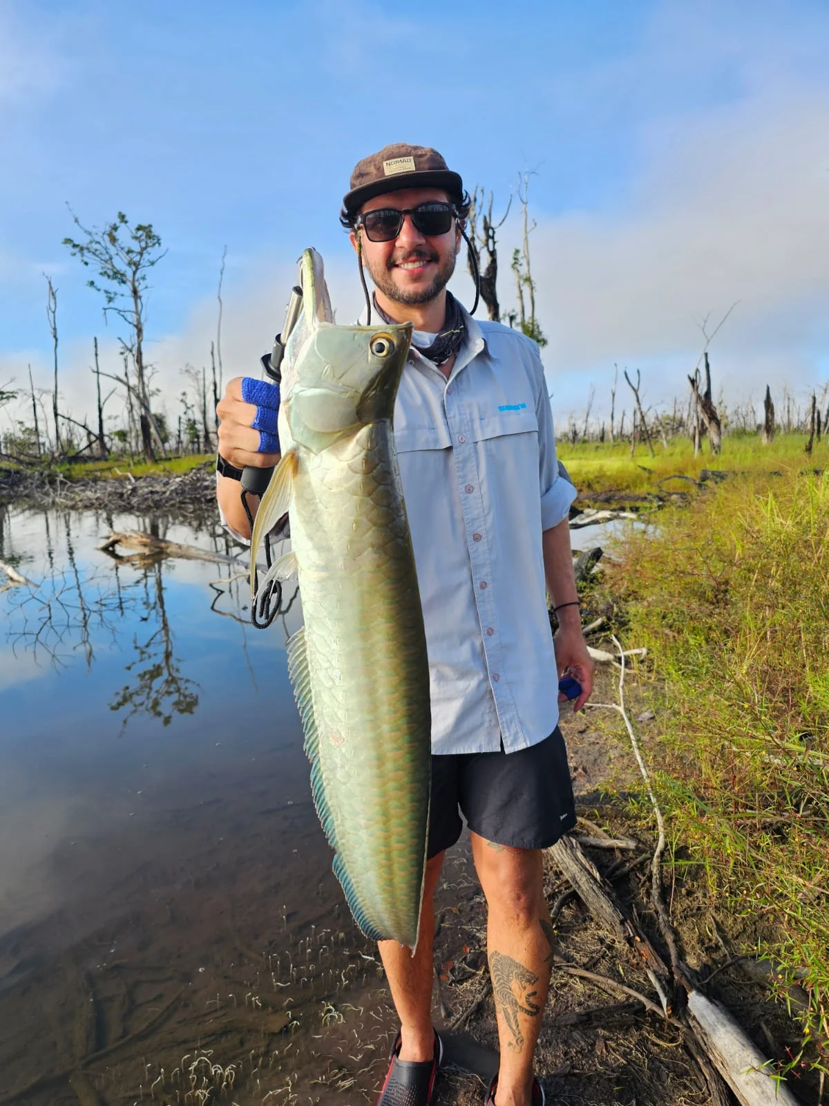 Pescador segura um grande peixe junto à margem do rio